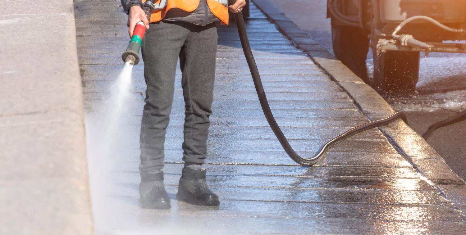 Worker cleaning driveway with gasoline high pressure washer splashing the dirt